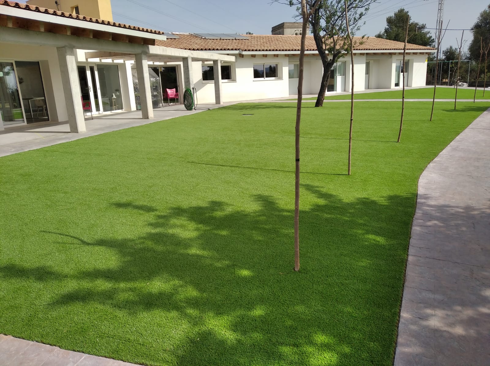 Amplio jardín delantero con césped artificial en vivienda moderna con porche acristalado