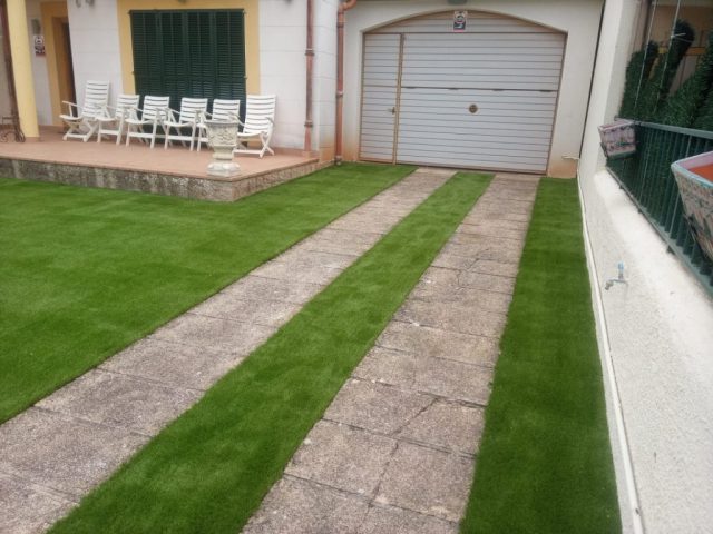 Entrada de casa con camino de baldosas rodeado de césped artificial recién instalado