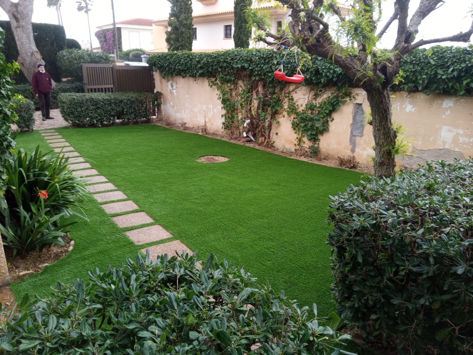 Jardín frontal con camino de losas y césped artificial alrededor de plantas y árboles
