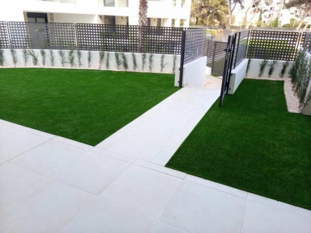 Entrada de vivienda con zonas de césped artificial separadas por un sendero pavimentado