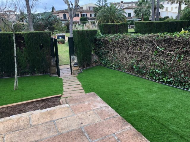 Jardín delantero con césped artificial junto a muro perimetral y puerta de acceso