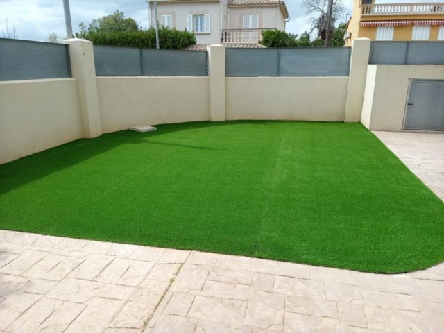 Espacio exterior residencial con césped artificial uniforme rodeado de muros beige